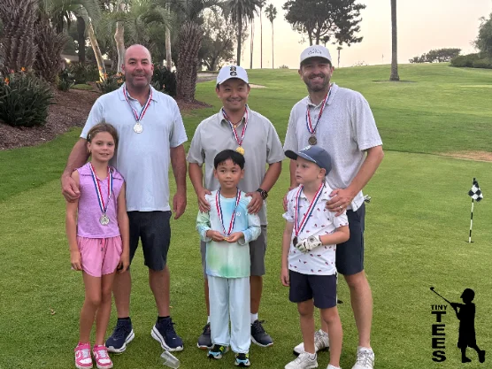 An adult-and-child tournament team posing with medals on the course