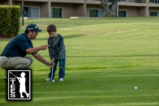 A coach kneeling to help a young player line up a putt